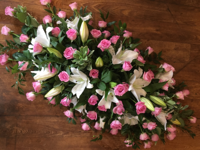 Tender Remembrance Casket Spray - Soft, graceful, and timeless, this casket spray is a touching expression of love and remembrance. It features a lush arrangement of blush pink roses interwoven with elegant white Oriental lilies, symbolizing purity, admiration, and eternal love. Accented with rich greenery and variegated foliage, the arrangement offers a classic, serene beauty. The combination of pink and white tones evokes a gentle, feminine spirit, making this an ideal tribute for honoring someone cherished with deep affection and tenderness.