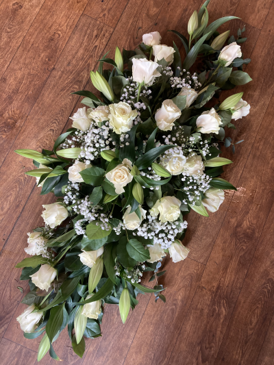 Heavenly Whisper Casket Spray - Graceful and serene, this casket spray features an elegant blend of ivory roses, unopened white lilies, and delicate baby’s breath (Gypsophila) nestled among lush, glossy greenery. The soft white tones evoke peace, remembrance, and purity, making it a fitting tribute for a loved one’s farewell. The arrangement’s gentle structure and fresh, natural beauty create a timeless expression of sympathy, comfort, and enduring love. Ideal for both traditional and modern services, this design honors a life with quiet dignity and heartfelt grace.